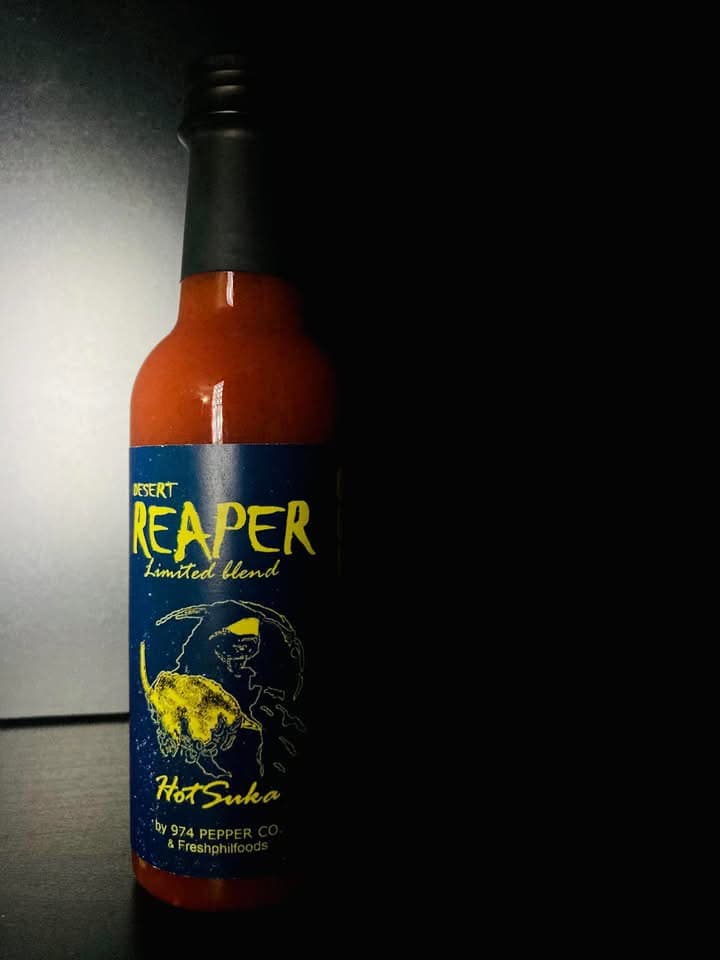 Dramatically lit bottle of Desert Reaper hot sauce with a blue and yellow label.